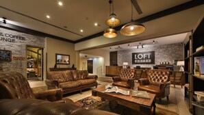 A spacious living room with leather sofas and armchairs, a coffee table, and a bookshelf. A sign indicates the presence of a coffee lounge. - Wilson Palace by LOFT (Bratislava)