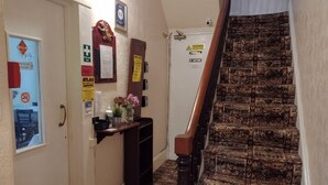 Corredor com escada, balcão de recepção e vários avisos, incluindo saída de incêndio e porta de acesso privativo.