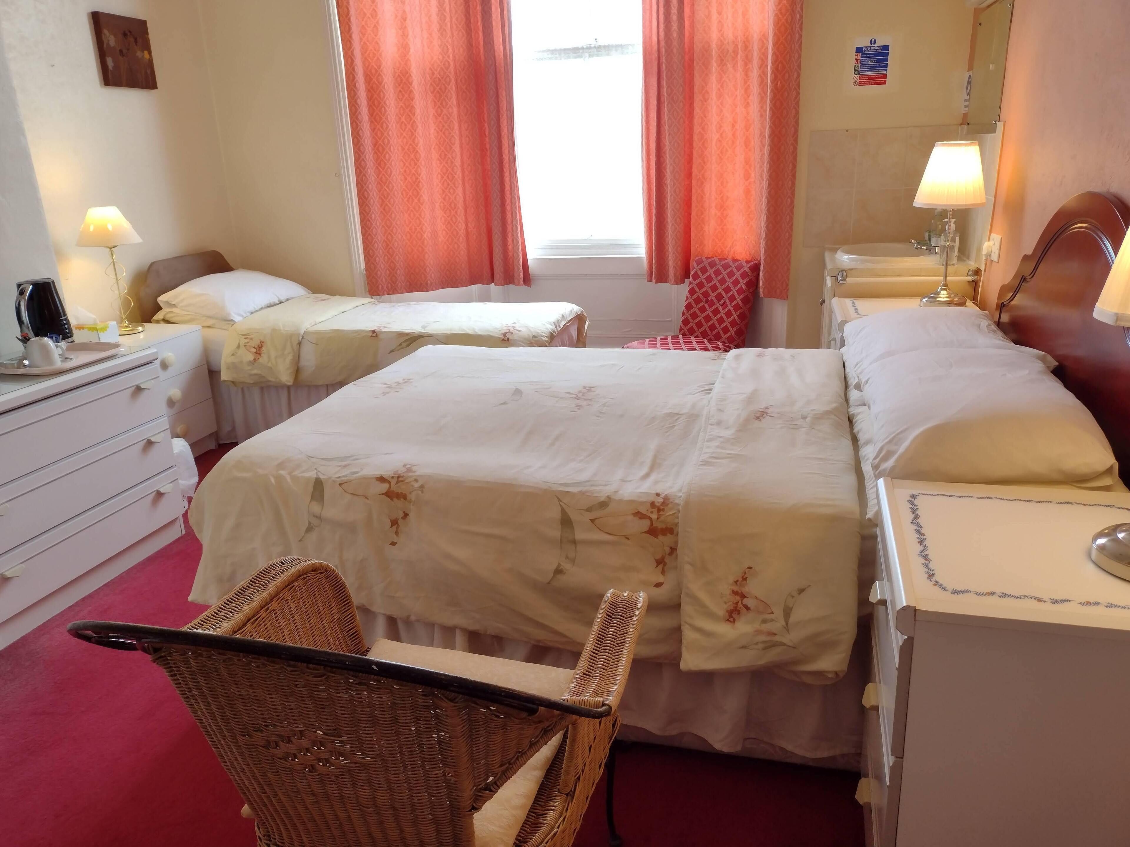 A hotel room with two beds, a chair, a desk, a lamp, and a window with curtains.