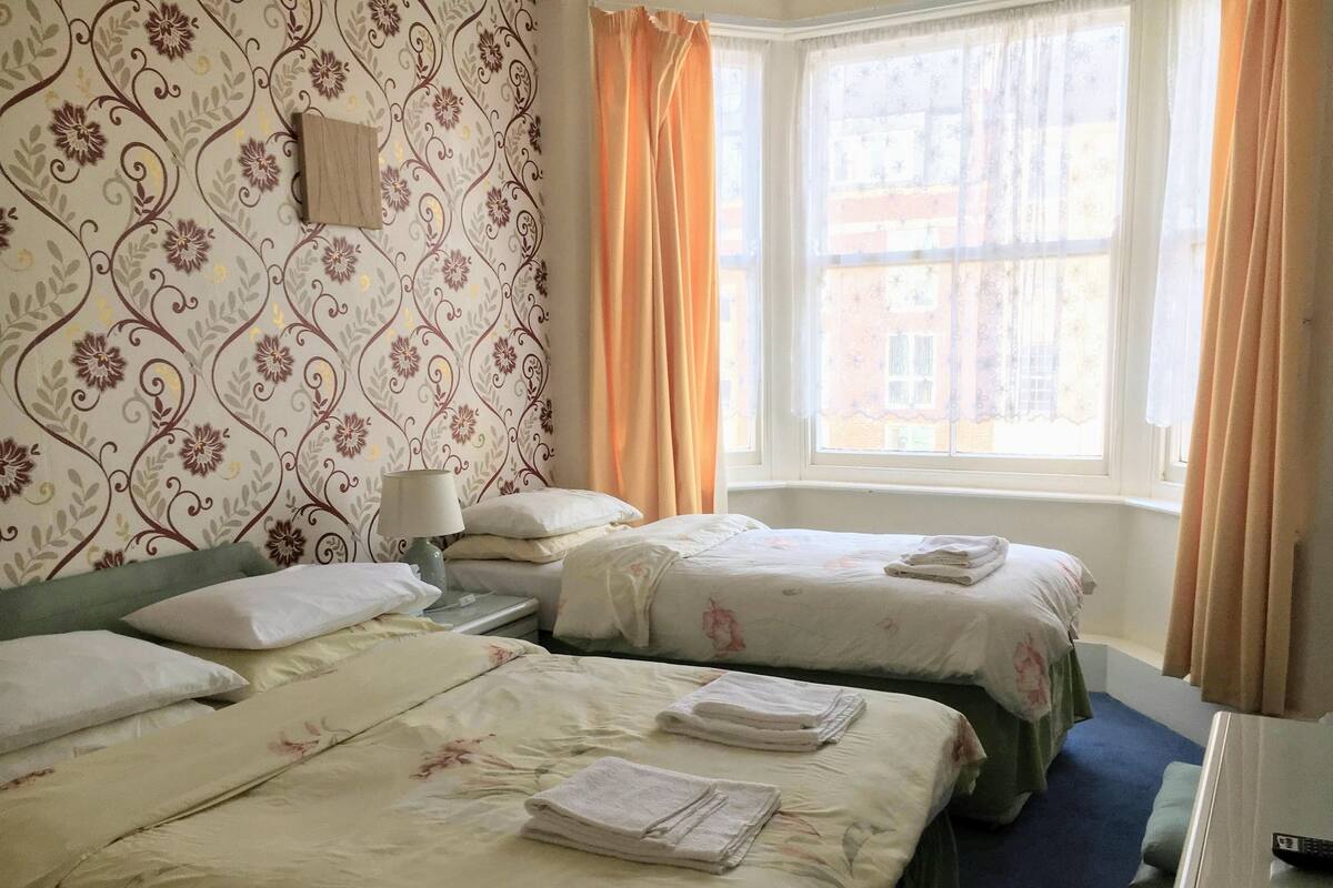 A hotel room with two beds, a nightstand, a lamp, and a window with curtains.