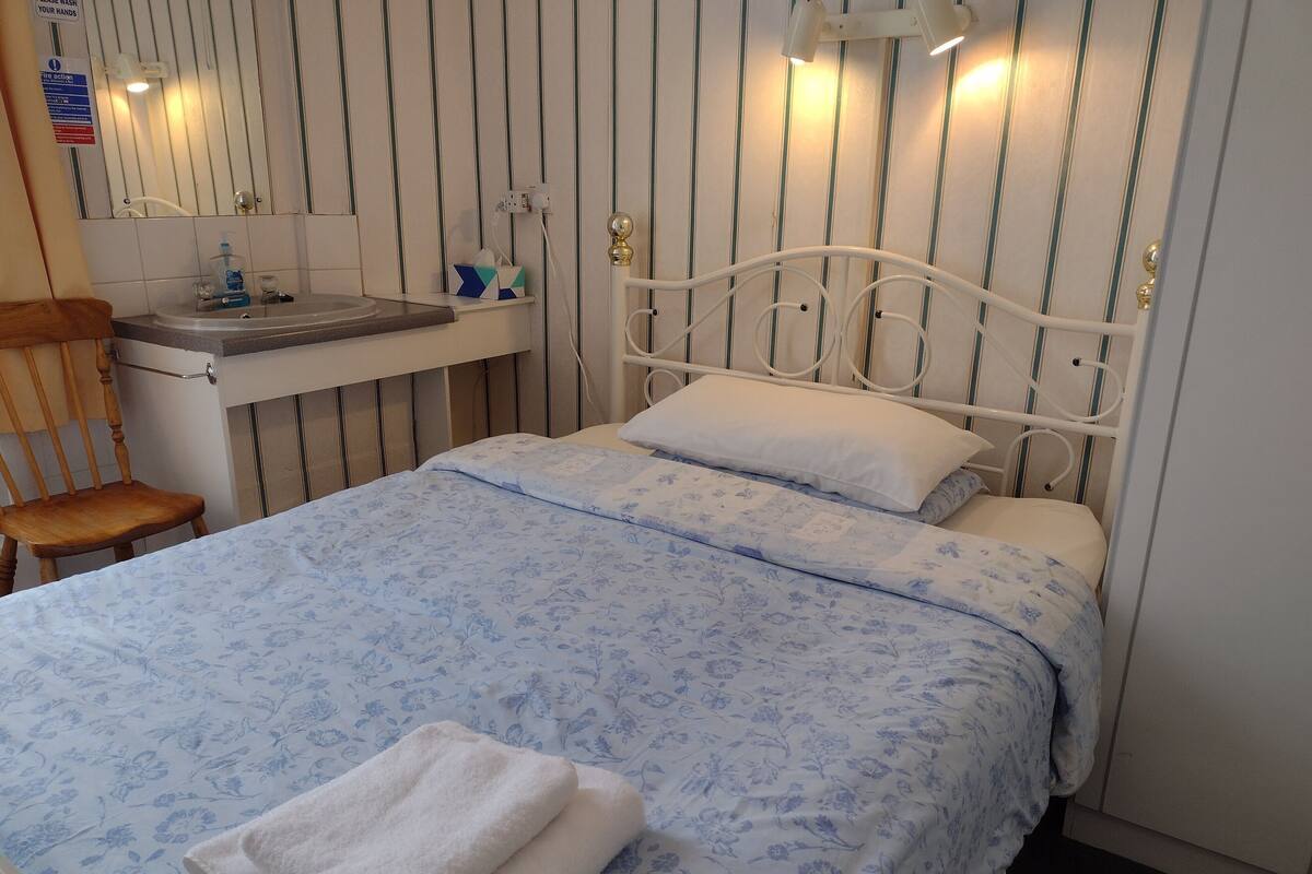 A bedroom with a bed, a chair, a bedside table, and a mirror.