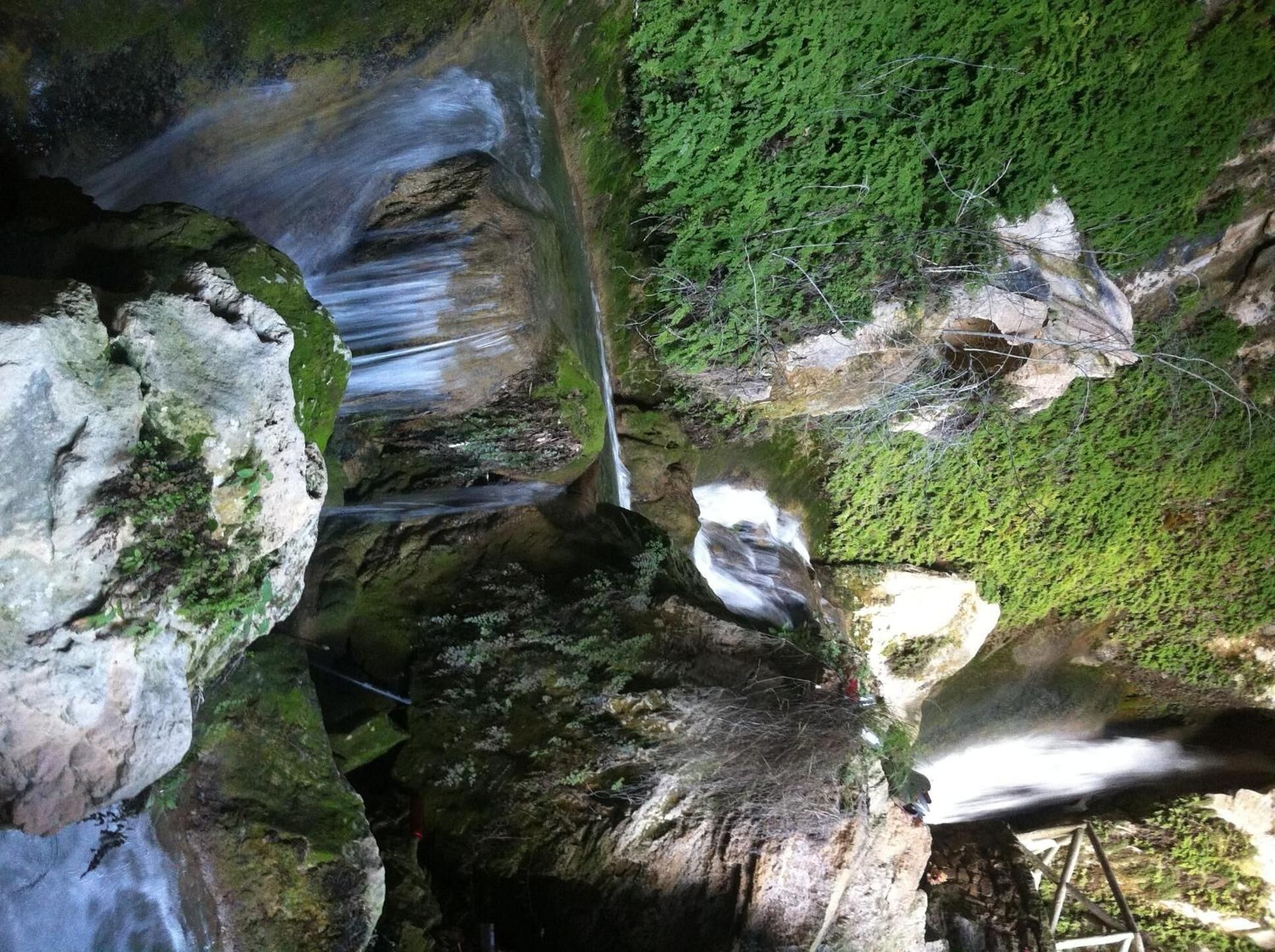 A natural rock formation with a waterfall and dense green foliage.