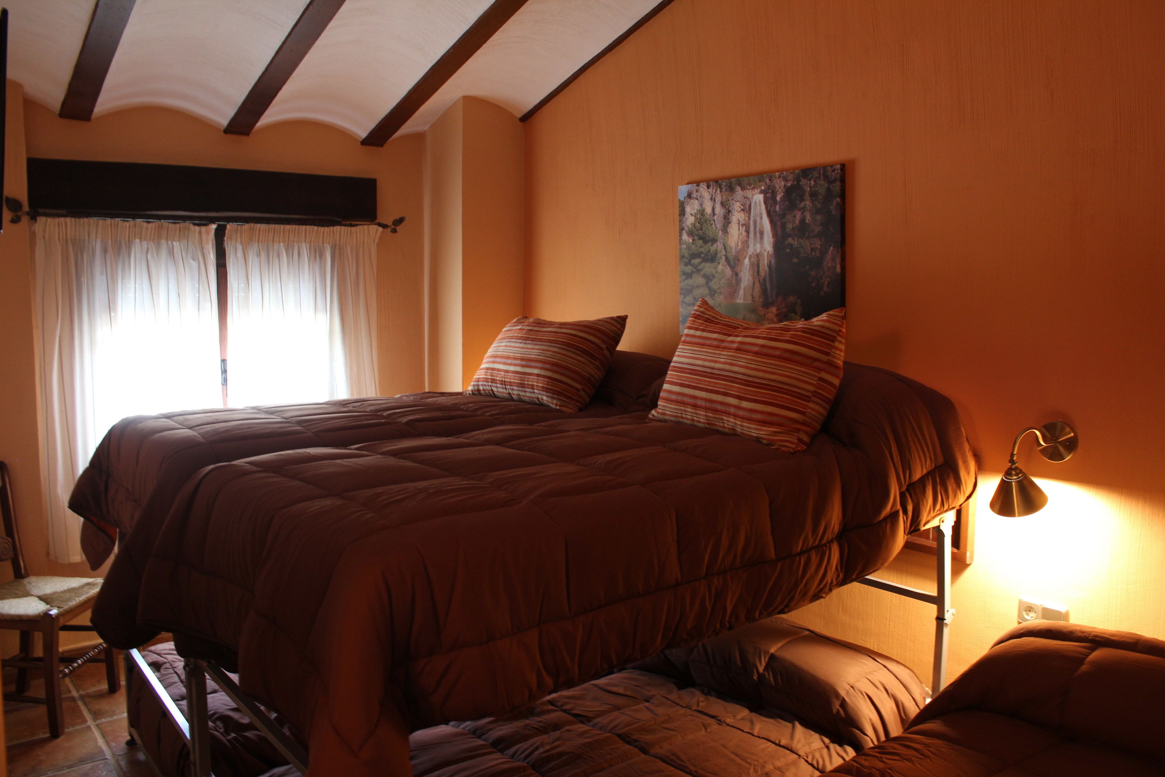Una cama doble con almohadas a rayas y un cabecero, una lámpara de noche y un cuadro de una cascada en la pared.