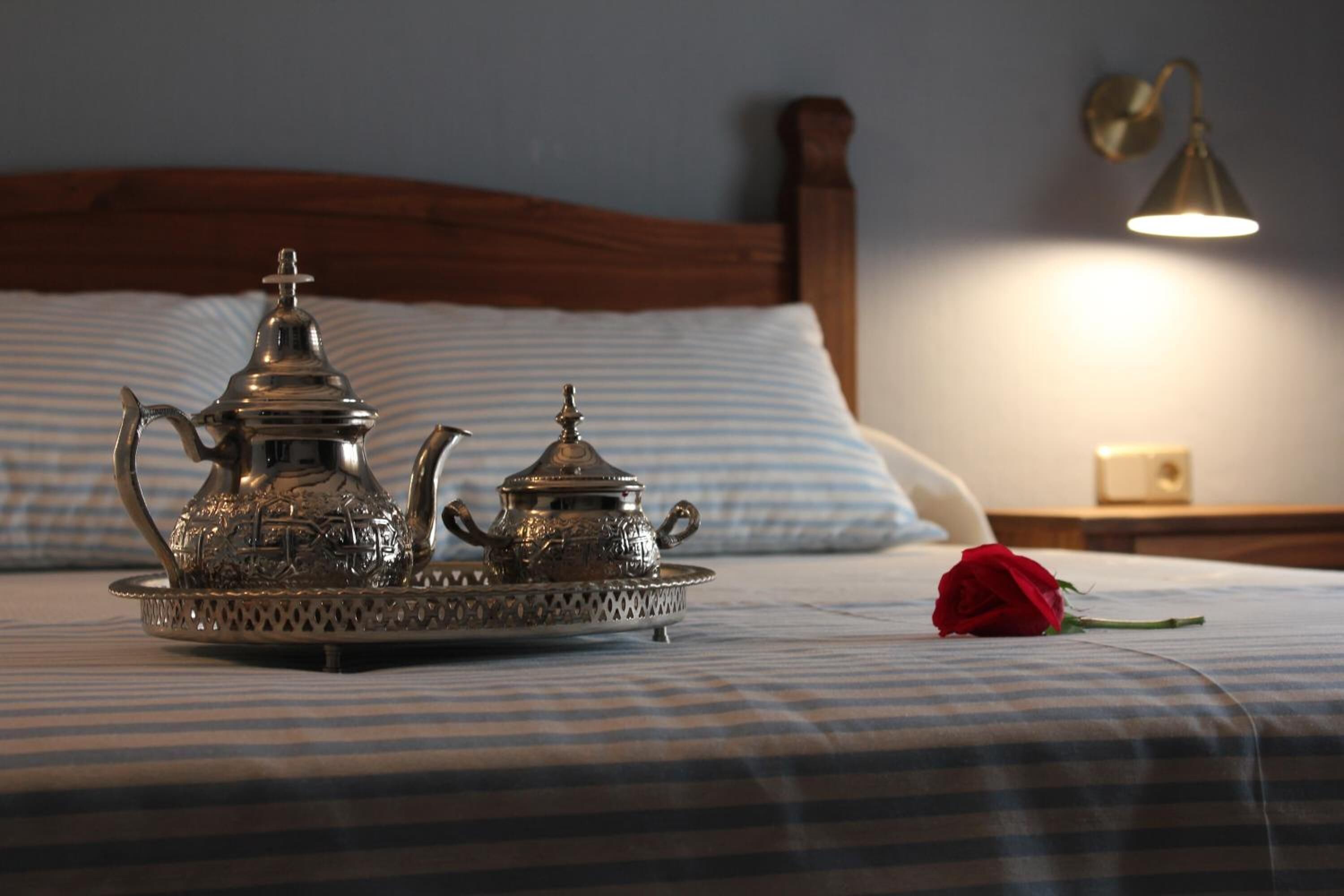 A neatly made bed with striped bedding, a decorative tray with silverware, and a single red rose.