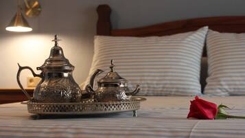 Ein Bett mit einem Metalltablett, das zwei kunstvolle Teekannen, eine einzelne Rose und eine Wandlampe beherbergt.
