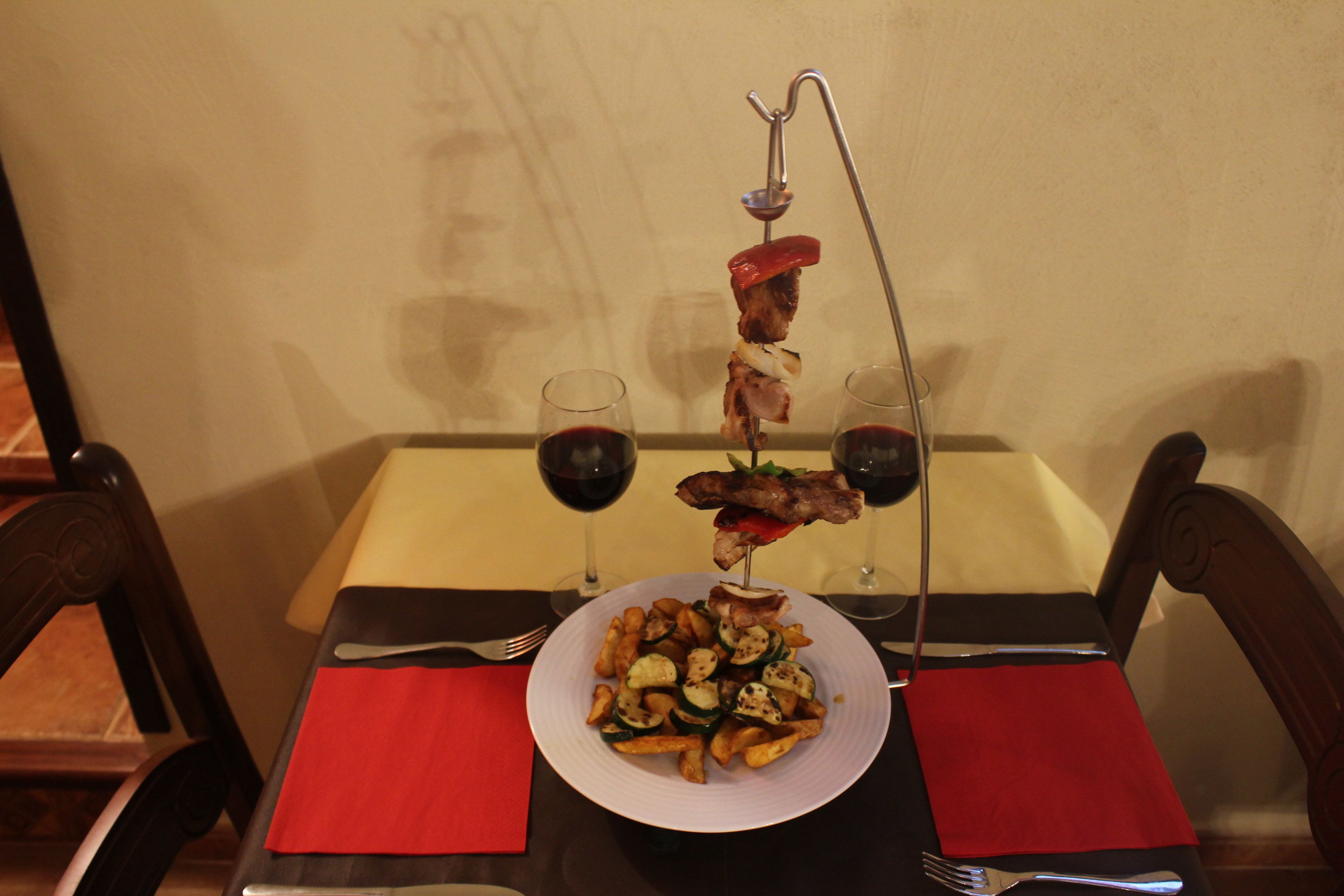 Une table à manger avec une assiette de nourriture, deux verres de vin rouge et une serviette rouge.