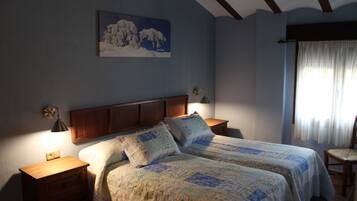 Un dormitorio con cabecera de madera, dos mesitas de noche, una cama con ropa de cama estampada, una lámpara de pared, una ventana con cortinas y un cuadro en la pared.