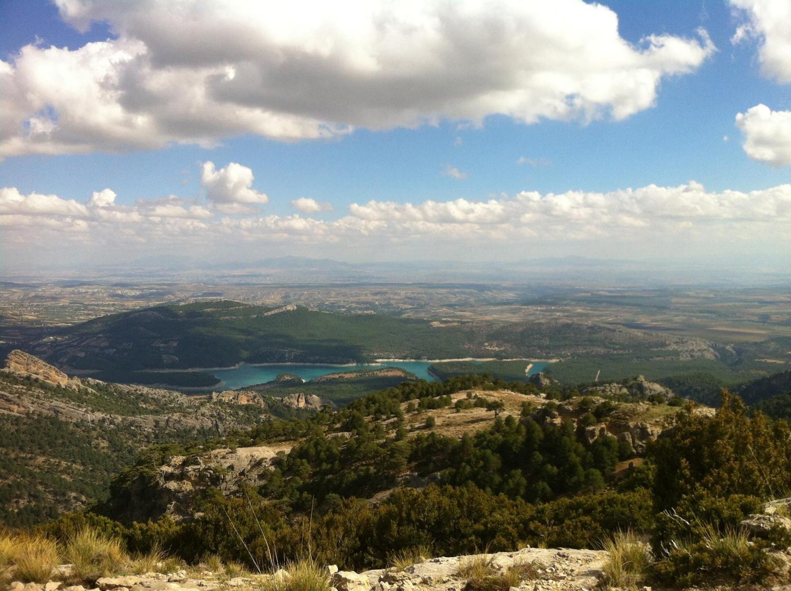 A panoramic view of a mountainous landscape with a lake and distant cityscape.