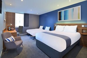 A hotel room with two beds, a desk with a lamp, a chair, and a large abstract painting on the wall. - Travelodge Ryde Isle of Wight (Ryde)