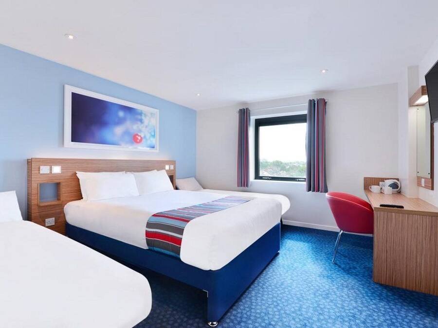 A hotel room with a large bed, a desk, a chair, and a window with curtains.