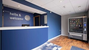 A reception area with a blue wall, a clock, a vending machine, and a patterned floor. - Travelodge Ryde Isle of Wight (Ryde)