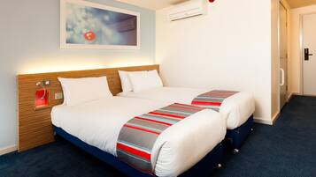 A hotel room with a bed, bedside controls, an air conditioning unit, and a door.