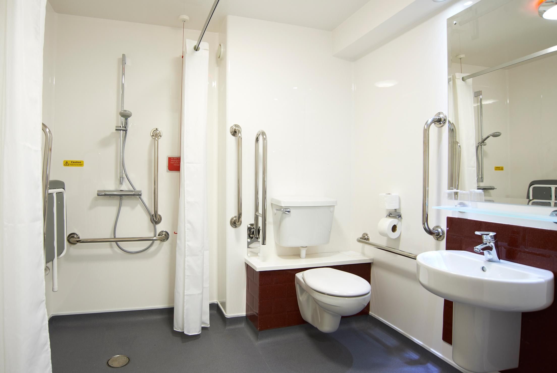 A bathroom with a toilet, sink, shower, and grab bars.