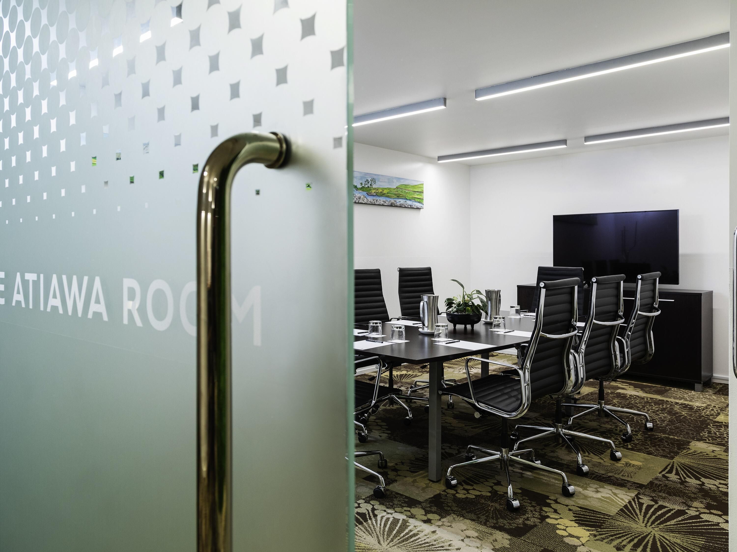 A conference room with a glass partition, a black leather conference table, and black office chairs.
