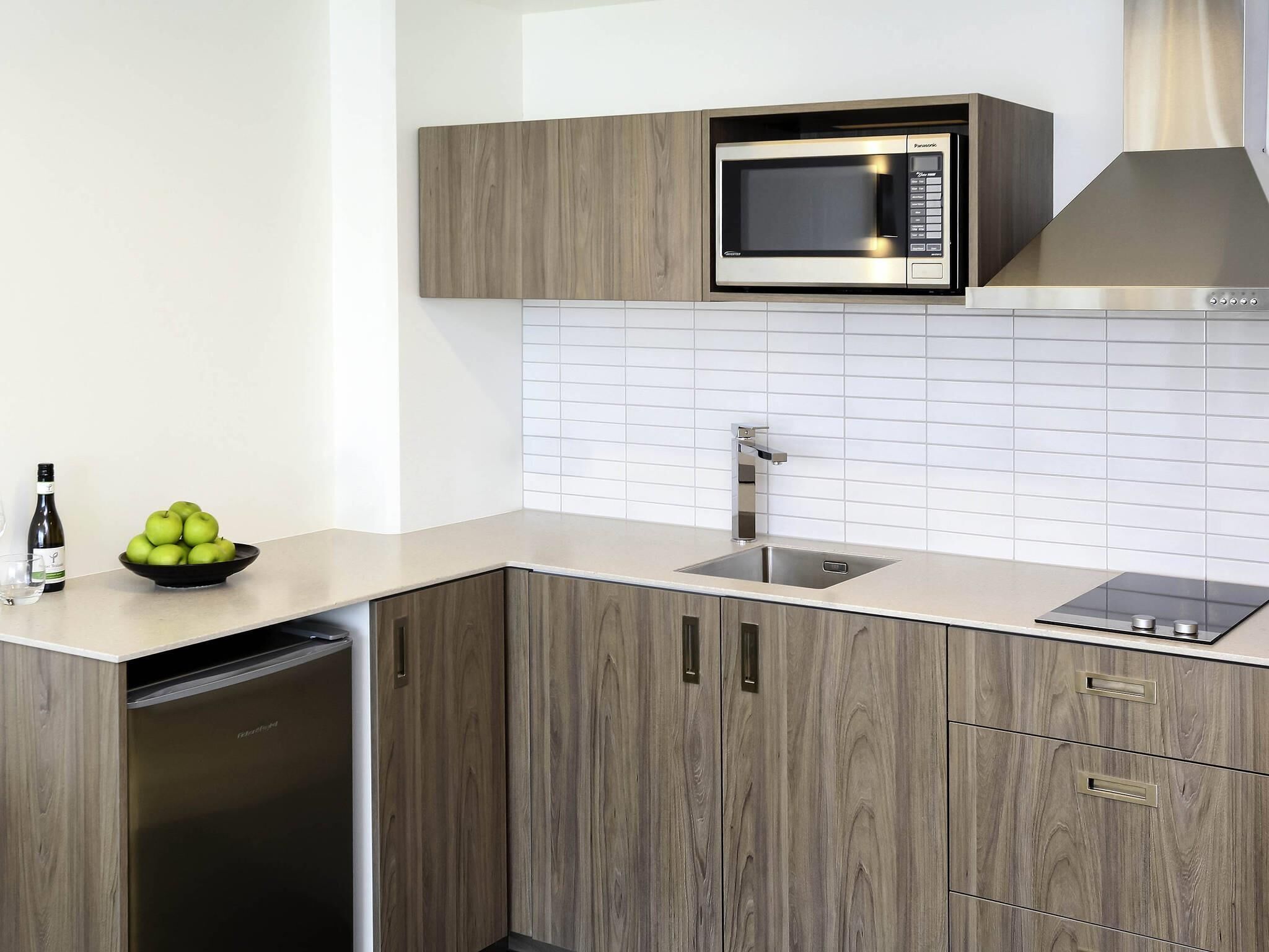 Una cocina moderna con microondas integrado, pileta de acero inoxidable y alacenas de madera.