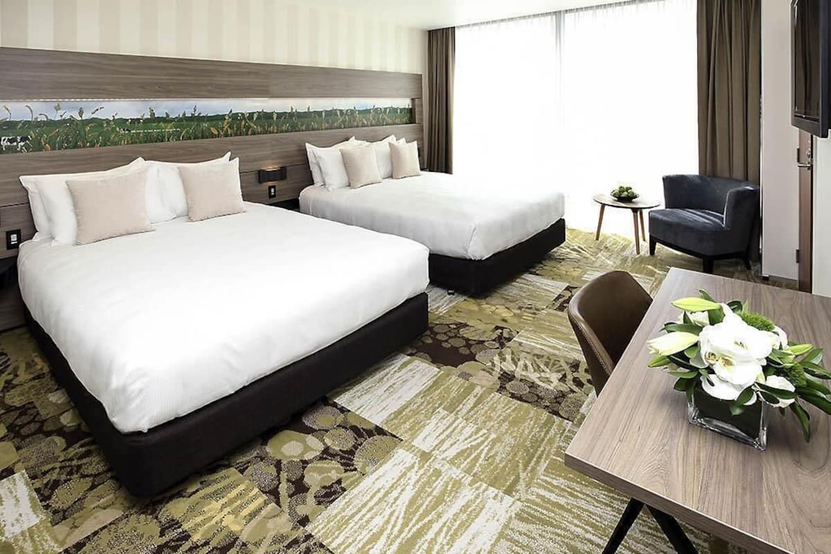 A hotel room with two beds, a desk, a chair, and a TV.