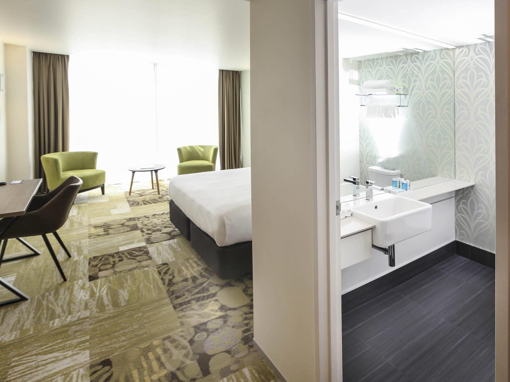 A hotel room with a bed, two chairs, a small table, a bathroom with a sink and toilet.