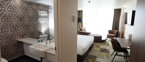 Habitación de hotel con baño, cama, escritorio y silla.