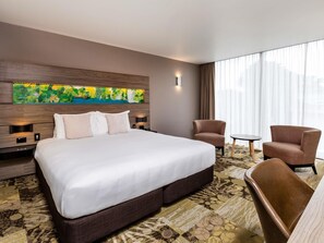 Habitación de hotel con una cama grande, dos sillones, una mesita y un ventanal con cortinas.
