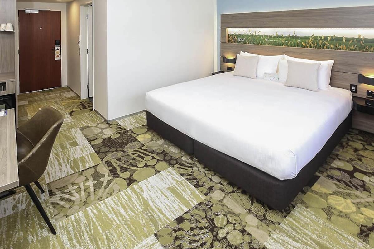 A hotel room with a large bed, a desk, and a chair.