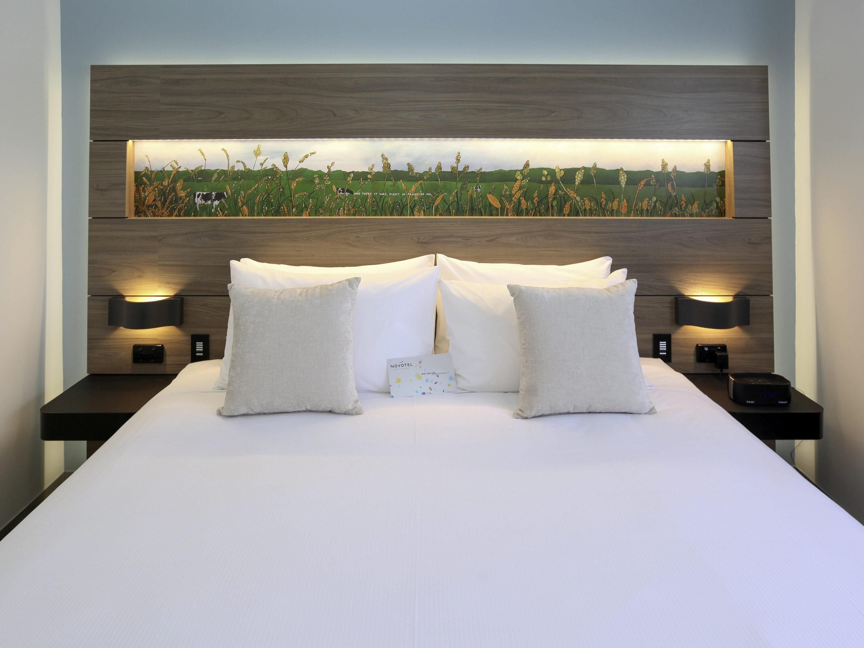 A bed with two pillows, a nightstand with a phone, and a wall-mounted lamp.