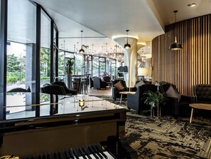 Un vestíbulo moderno con un piano de cola, zonas de estar y grandes ventanales que ofrecen vistas al exterior.
