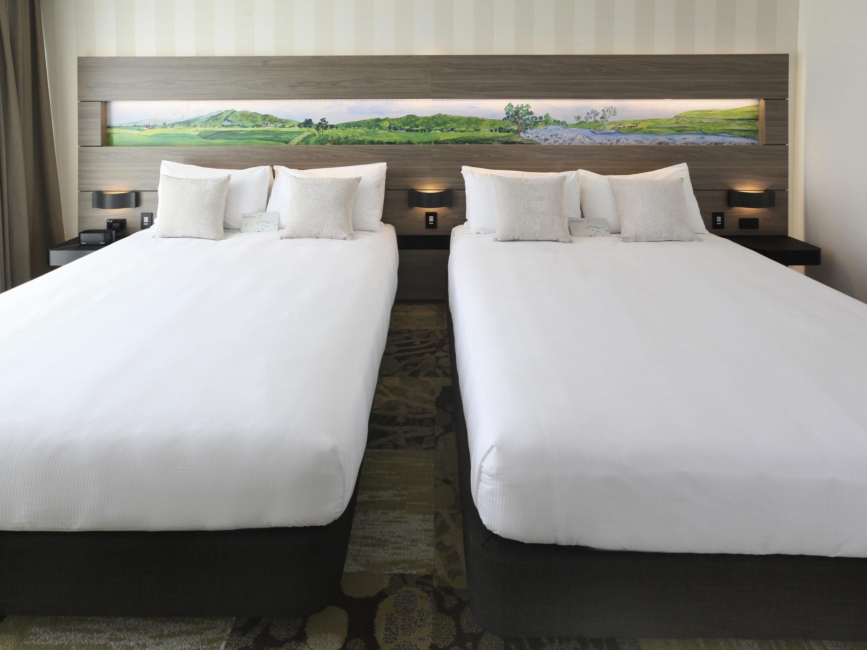 A hotel room with two beds, a large painting above the beds, and a nightstand with a lamp.