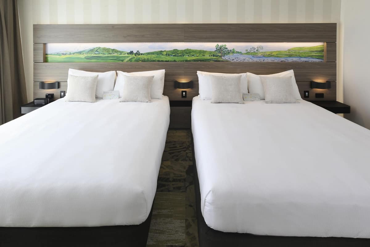 A hotel room with two beds, a large painting above the beds, and a nightstand with a lamp.