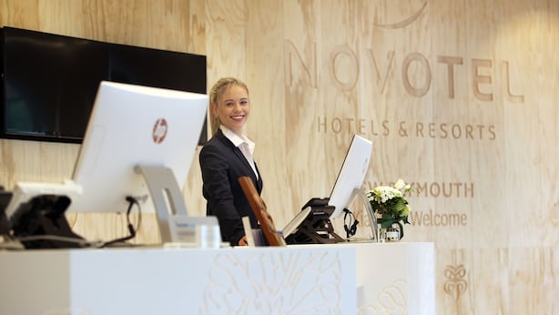 Un mostrador de recepción en Novotel Hotels & Resorts con una computadora, un teléfono y un cartel de bienvenida.