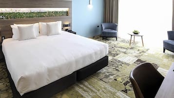 A hotel room with a large bed, a chair, a small table, and a view of a field through the window.