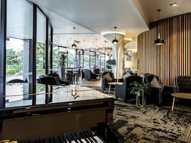 Un vestíbulo moderno con un piano de cola, zonas de estar y grandes ventanales que ofrecen vistas al exterior.