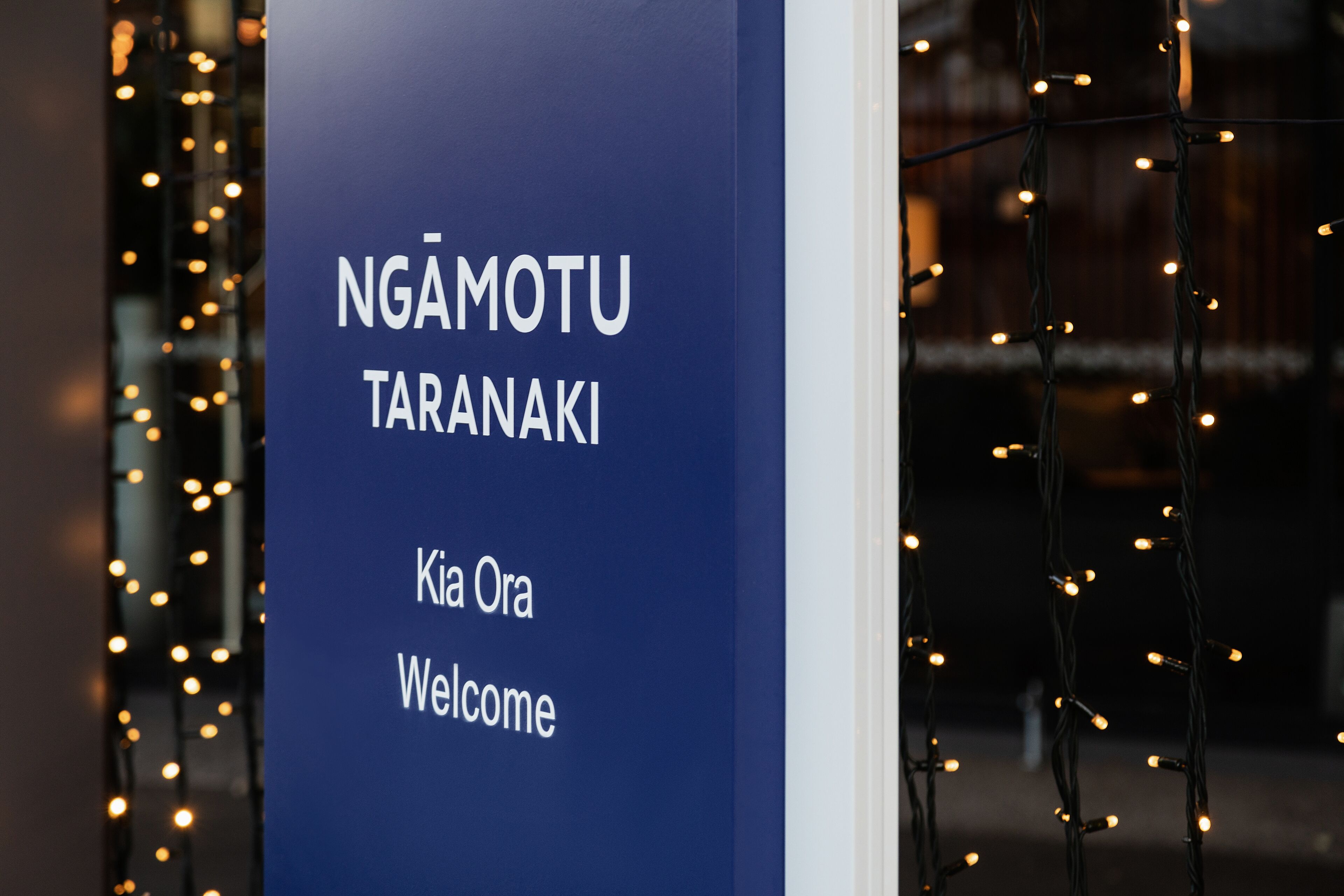A sign with "NGÂMOTU TARANAKI" and "Kia Ora Welcome" in white text on a blue background.