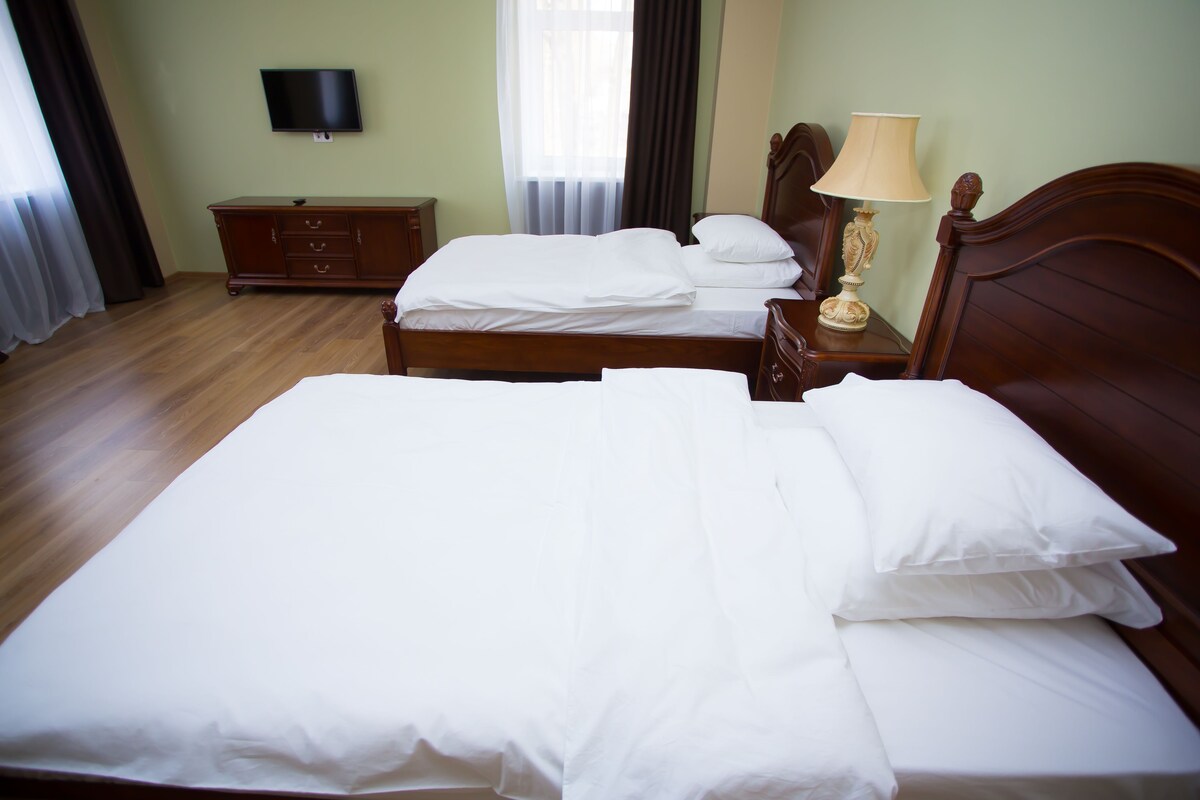 A hotel room with two single beds, a wooden dresser, a television on the wall, and a lamp on the dresser.