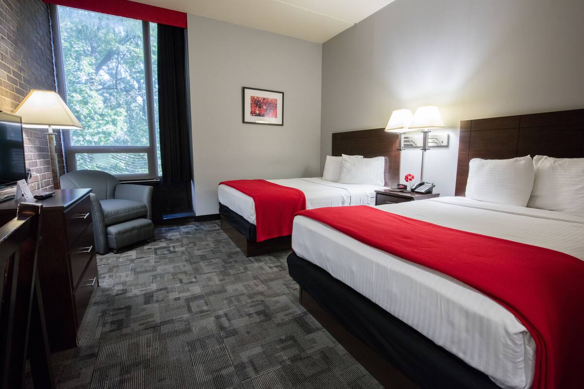 Ein Hotelzimmer mit zwei Betten, einem Schreibtisch, einem Stuhl und einem großen Fenster.