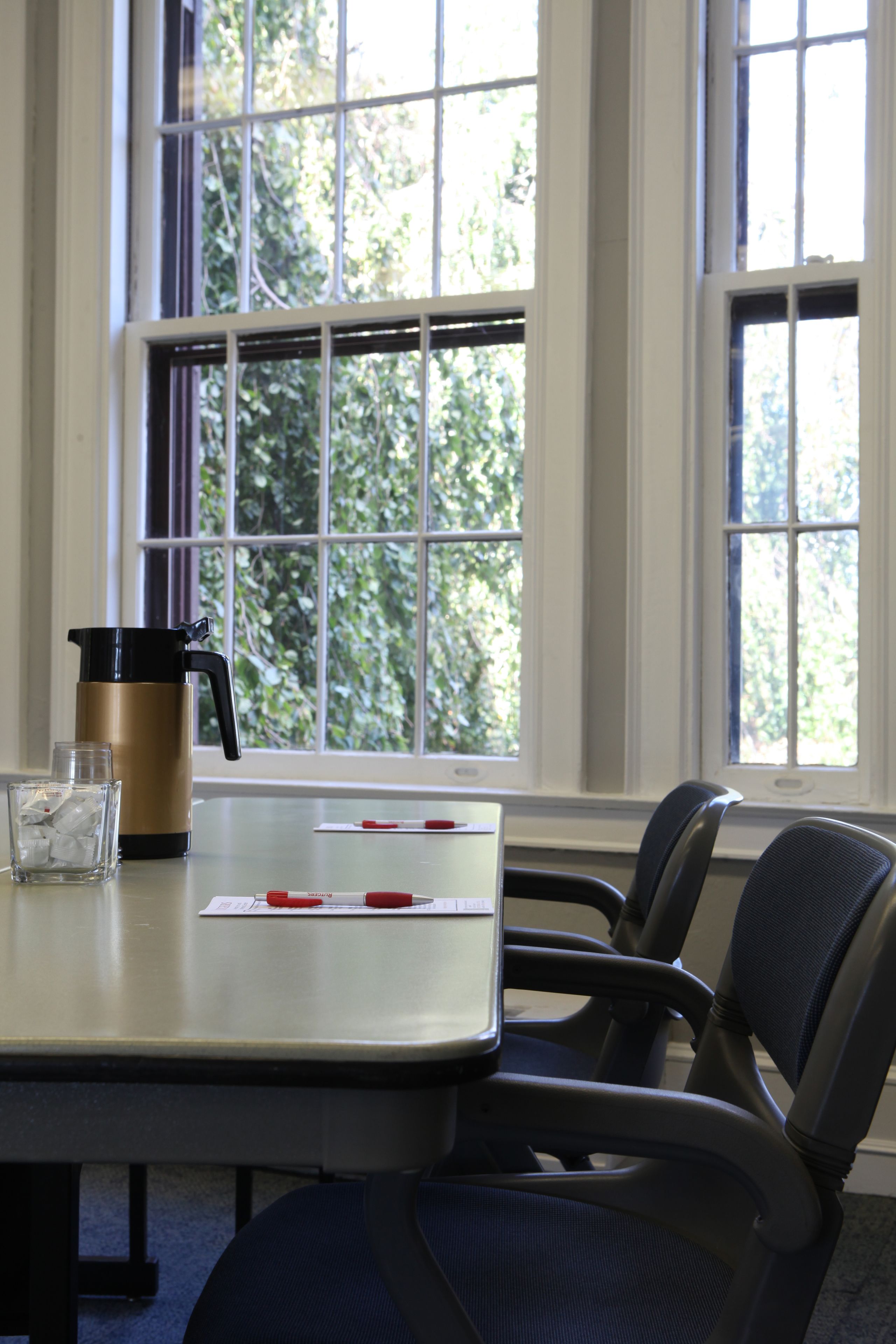 A conference table with a coffee maker, a glass of water, and a notepad.
