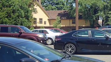 A parking lot with several cars, including a black sedan and a white sedan, parked in front of a yellow building with a chimney.