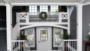 A two-story building entrance with a white door, a balcony with a wreath, and potted plants. - Rutgers University Inn and Conference Center (New Brunswick)