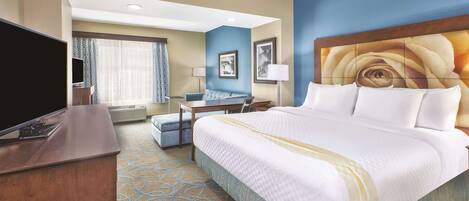 A hotel room with a large bed, a desk, a television, and a window with curtains.