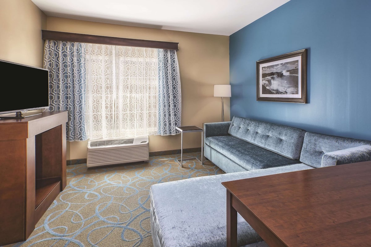 Een hotelkamer met een flatscreen televisie, een bank, een tafel en een kamerbreed tapijt met dessin.