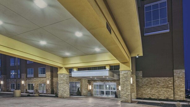 Een hotelentree met een overdekte doorgang, een bord met La Quinta Inn & Suites, en een gevel van steen en baksteen.
