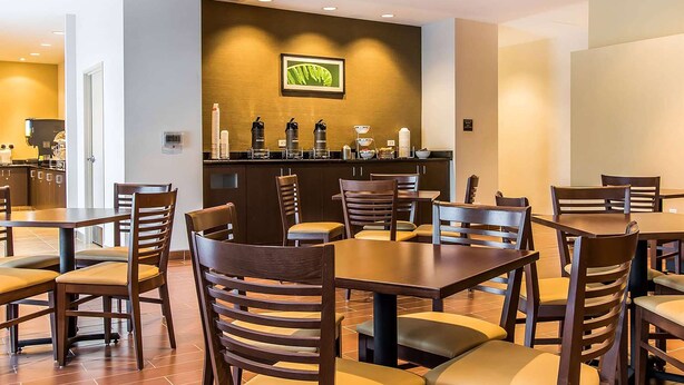 A restaurant with wooden tables and chairs, a counter with coffee machines, and a framed picture on the wall. - Wingate by Wyndham Jonesboro/Hodge (Jonesboro)