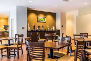 A restaurant with wooden tables and chairs, a counter with coffee machines, and a framed picture on the wall.