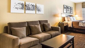 A hotel room with a sofa, a coffee table, a bed, and wall art. - Wingate by Wyndham Jonesboro/Hodge (Jonesboro)