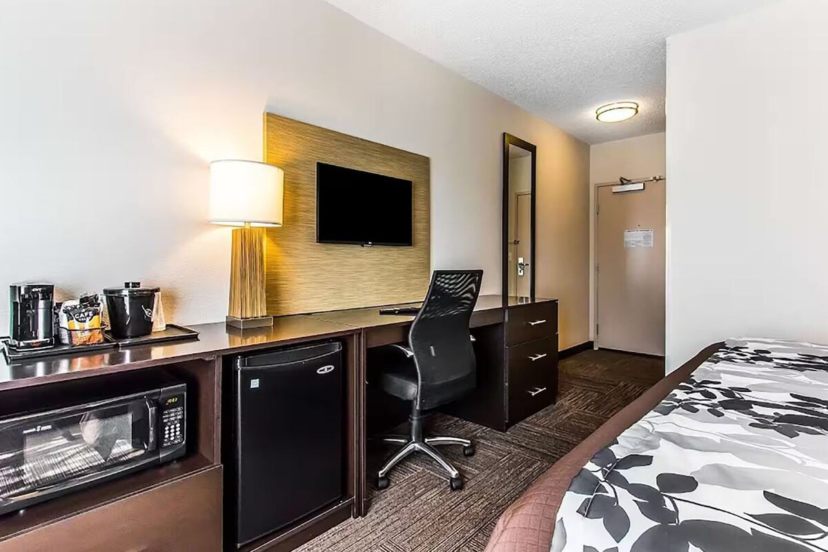 A hotel room with a desk, a television, a microwave, a coffee maker, and a bed.