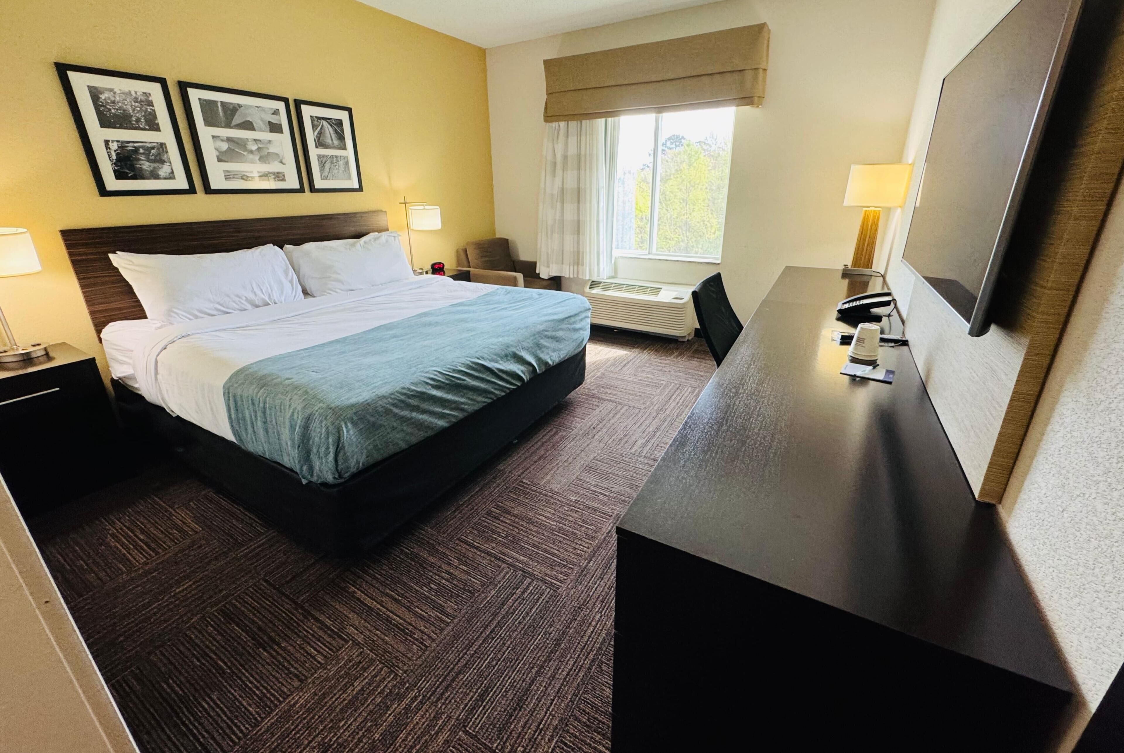 A hotel room with a bed, bedside tables, a desk, a television, and framed pictures on the wall.