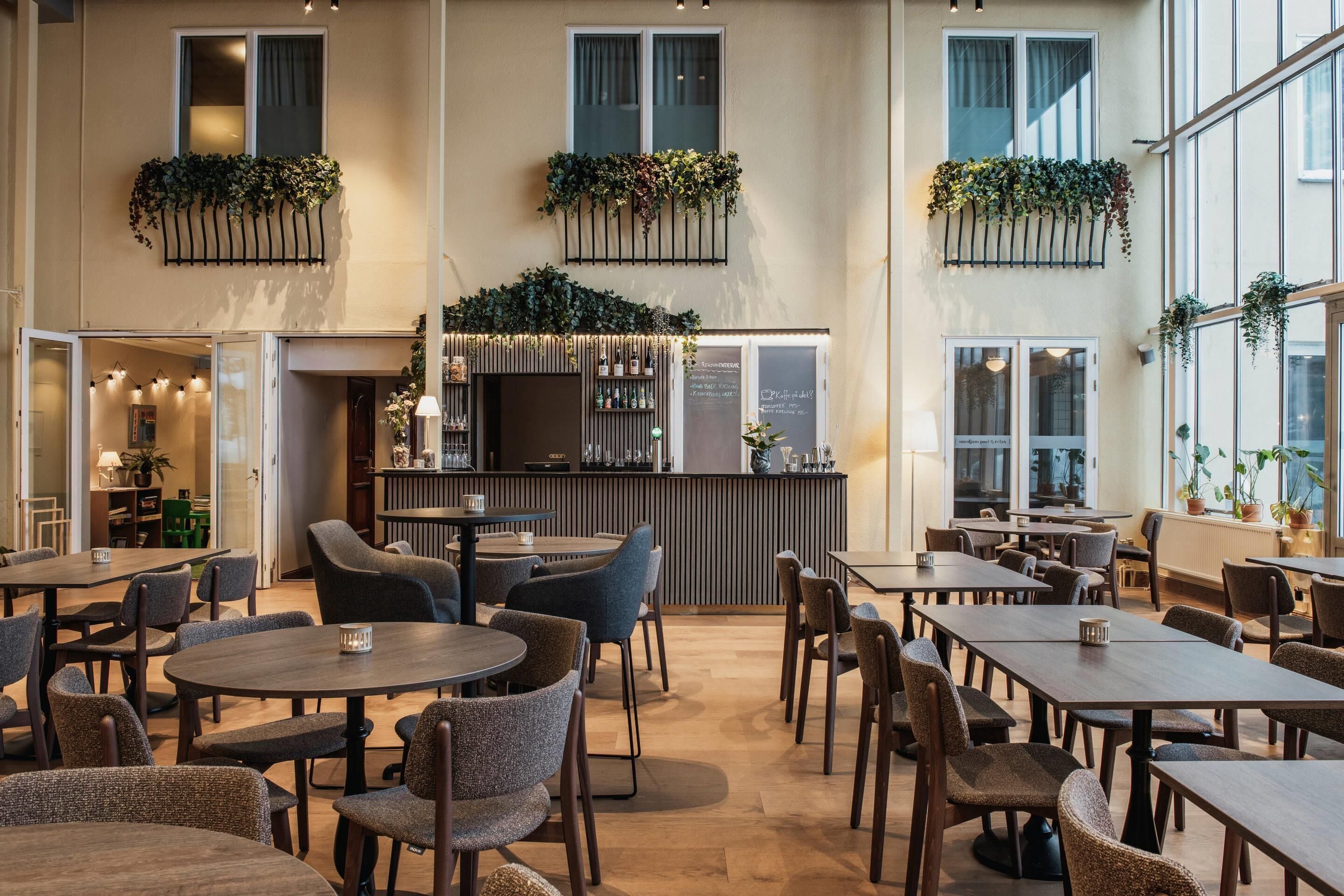 A spacious indoor dining area with multiple tables and chairs, a bar with a wooden counter, and large windows allowing natural light.