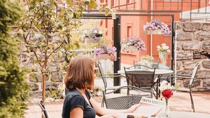 Eine Frau sitzt in einem Straßencafé an einem Tisch mit Stühlen und einer Speisekarte.