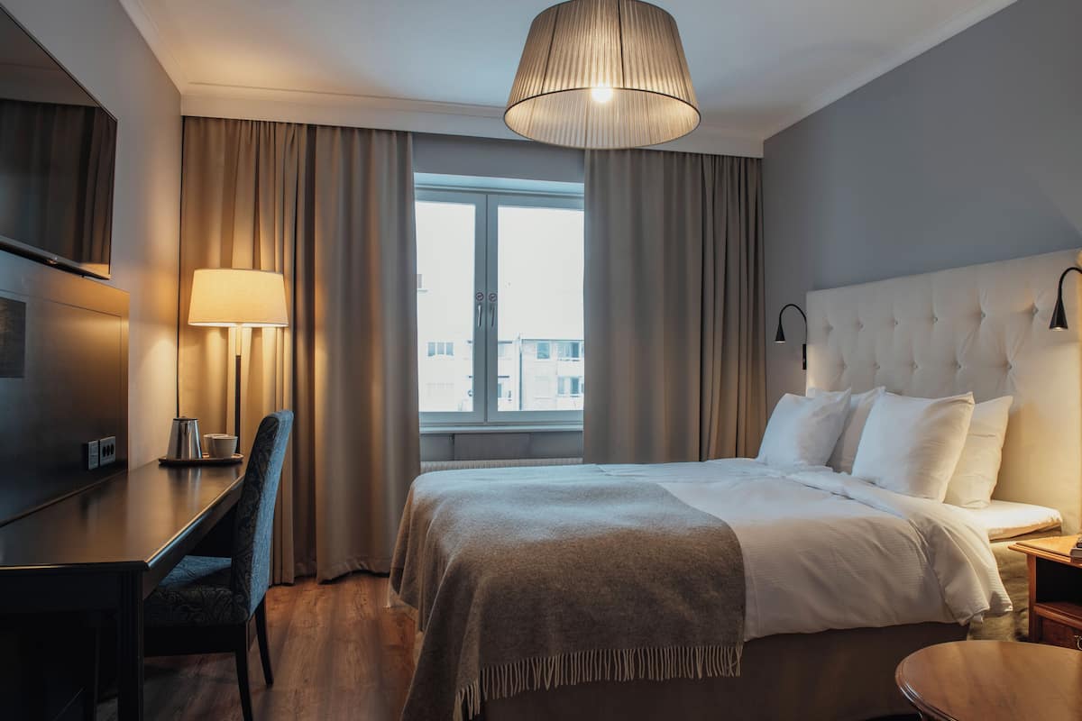 A hotel room with a bed, a desk, a chair, a TV, and a window with curtains.