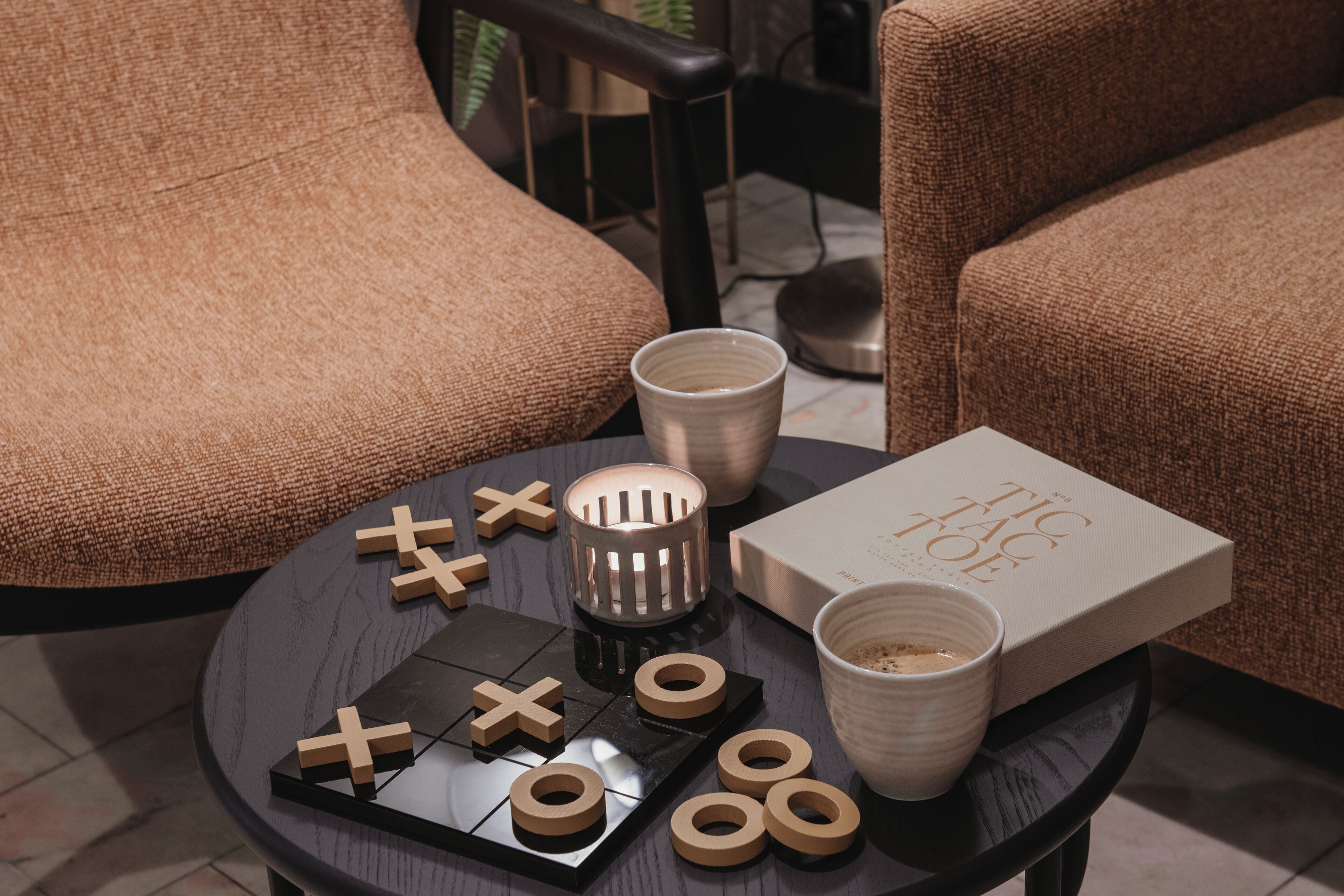 Een tafel met een potje tik-tak-toe, twee bekers, een kaars en een boek getiteld 'The Tic Tac Toe'.