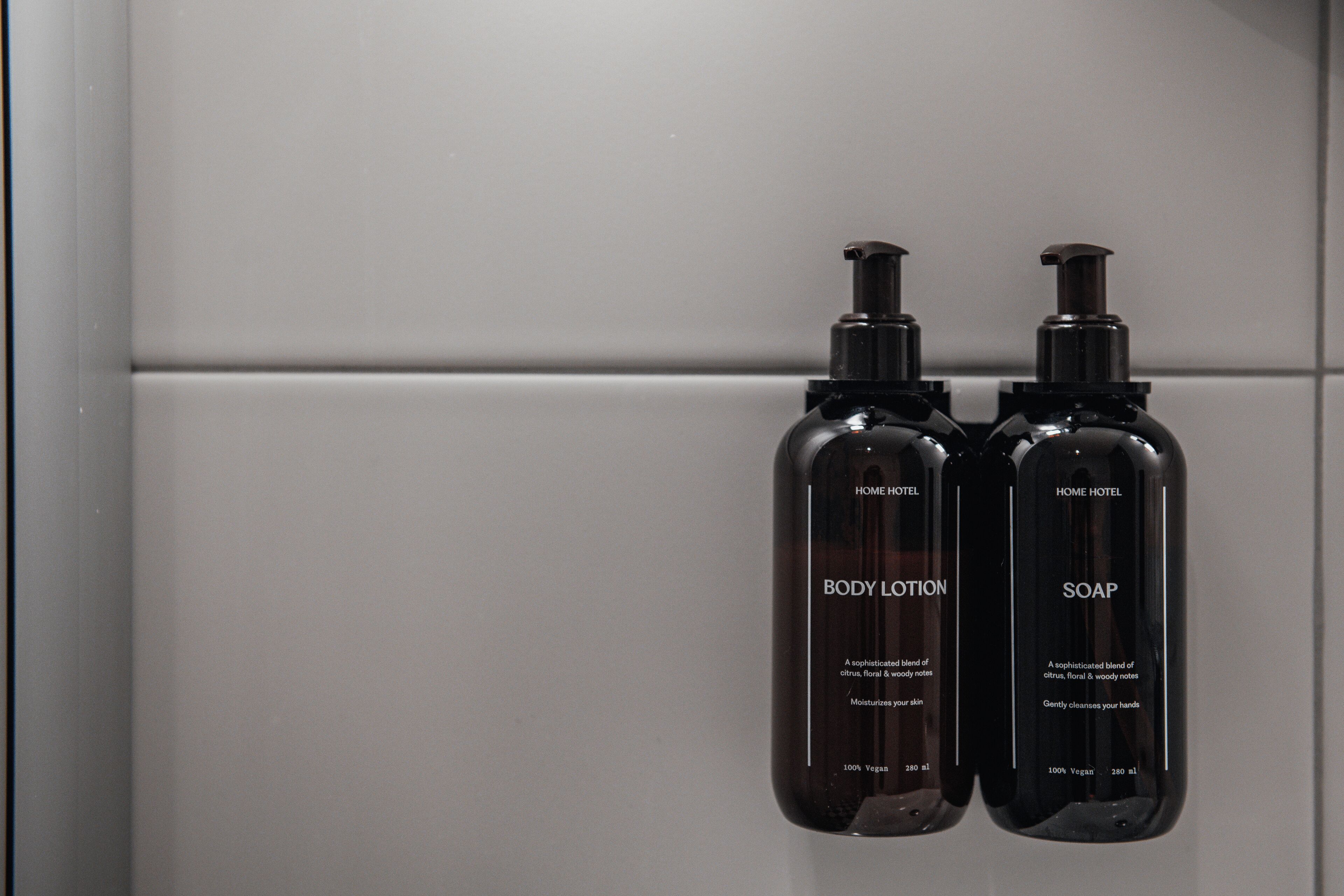 Two black bottles labeled "BODY LOTION" and "SOAP" with pumps, placed on a white surface.